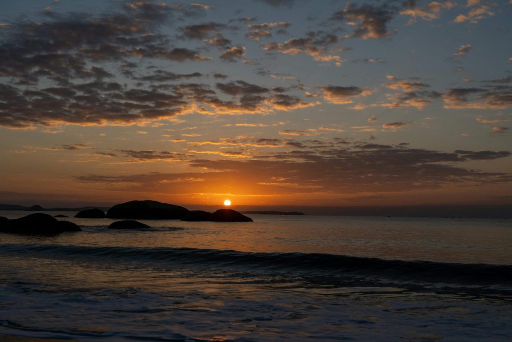 Friedlicher Sonnenaufgang über dem Meer mit der Silhouette von Felsen und einem leuchtenden Himmel.